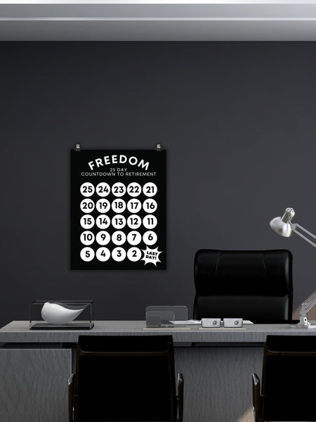 On a dark grey wall above a computer desk is a black 25-Day Countdown to Retirement Sign, 12 inches  by 16 inches and 16 inches by 20 inches. 25 white circles with black numbers countdown from 25 to the last day.