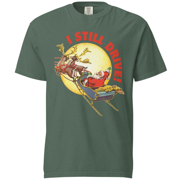 Product mockup of a green/blue tshirt with a vintage Santa Claus driving his sleigh and two deer across a moon. Above the moon text says, I still drive!