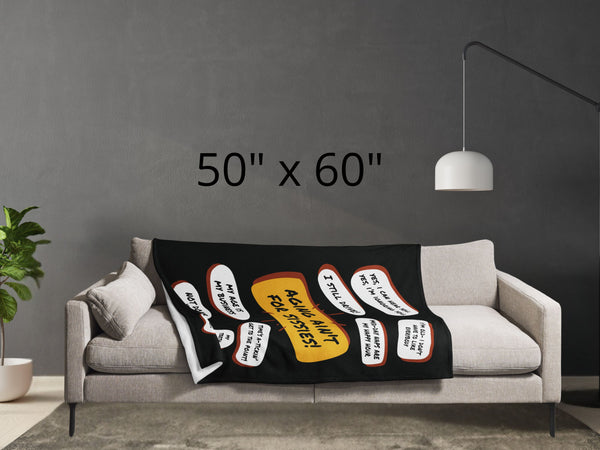 Lying across a grey couch is a large black throw blanket with a large yellow quote bubble in the center that says, Aging Aint For Sissies, Several quotes surround the center quote with several funny old people quips. Size is 50 by 60 inches.