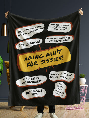 In front of a dark grey wall a person is holding up a large black throw blanket with large red yellow bubble in the center that says, Aging Aint For Sissies. Several white quote bubbles surround it with several funny old people quips. Free shipping.