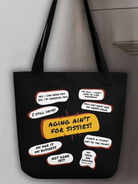 Hanging on a white door is a black tote bag with several funny old people bubble quotes, including, Aging Ain't For Sissies, I Still Drive, Not Done Yet, and several more.