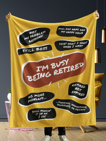 In front of a dark grey wall a person is holding up a large yellow throw blanket with a large red quote bubble in the center that says, I&#39;m Busy Being Tired. Several black quote bubbles surround the center quote with several funny old people quips.