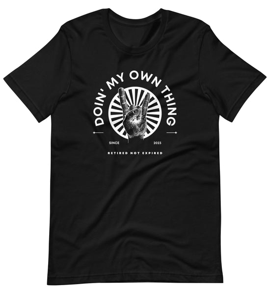 Image of a black tee with white text overlay that says, "doin' my own thing since 2023, retired not expired." A graphic image of rock 'n' roll hand sign in front of white starburst image is in the center.