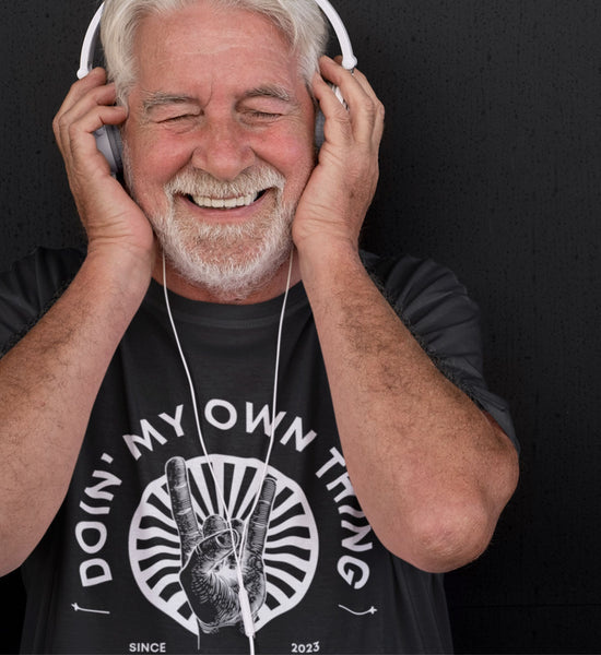 Image of an older man with white hair and beard rockin' out listening on headphones and wearing  a black tee with white text overlay that says, "doin' my own thing since 2023, retired not expired." A graphic image of rock 'n' roll hand sign in front of white starburst image is in the center.