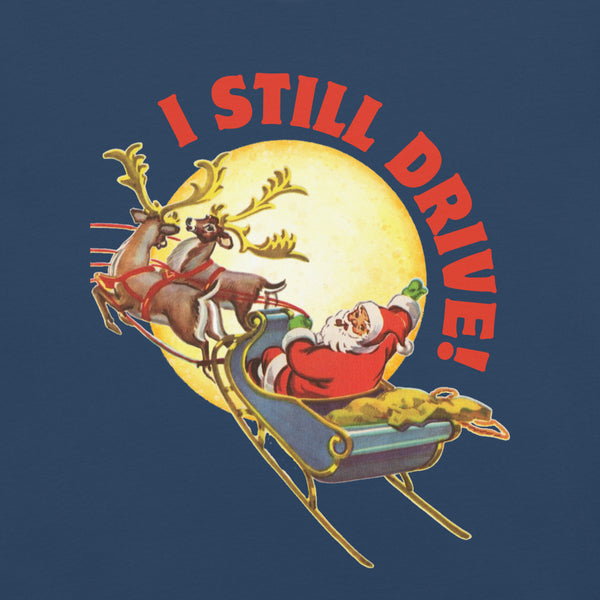 Close up detail the  grapic on a blue tshirt with a vintage Santa Claus driving his sleigh and two deer across a moon. Above the moon text says, I still drive!